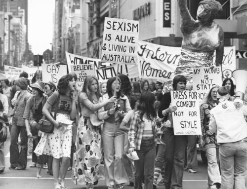 Black and white photo of International Women's Day Rally in Melbourne, March 8, 1975. The marchers hold picket signs, with statements including: "Sexism is alive and living in Australia", "My womb is not state property", "Dress for comfort not for style", "Believe in your own strength, women".