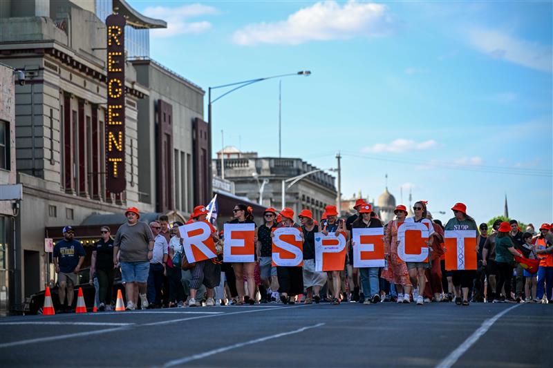 A crowd walks down a main street in Ballarat. People in the front carry large orange and white letters that spell 'RESPECT.'